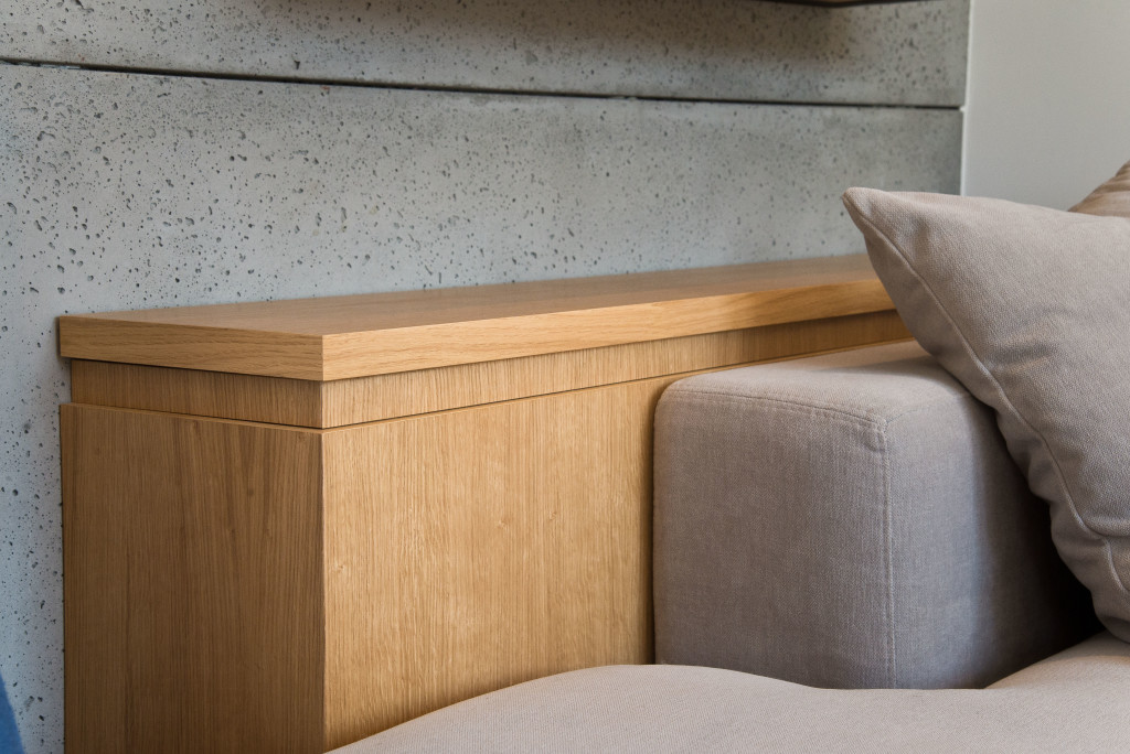 Imitacja betonu na ścianie, drewniany regał, szara tapicerka - kwintesencja skandynawskiego stylu